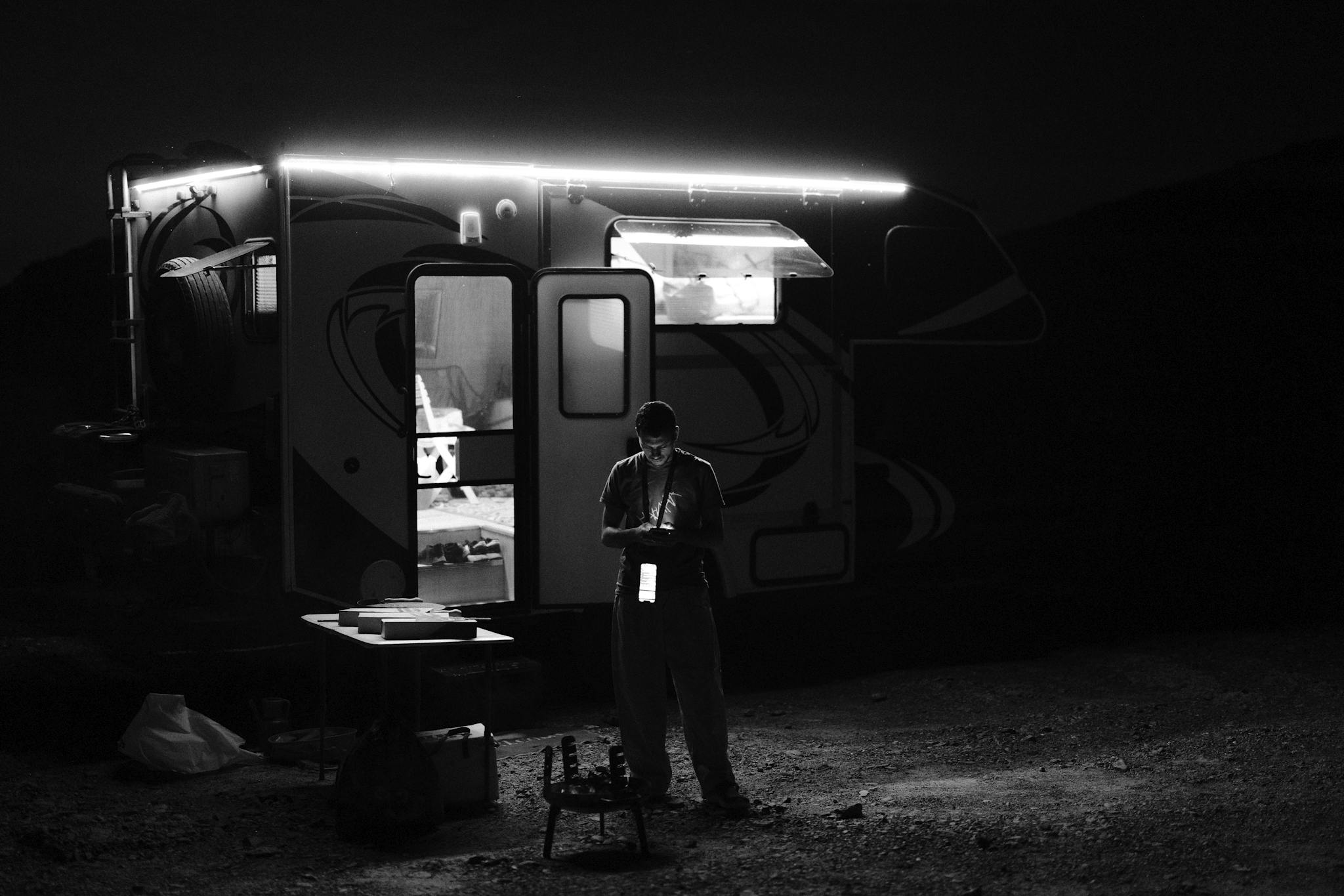 A solitary camper in a park illuminated by an RV at night trying to find RV repair near me.
